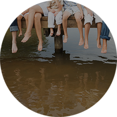 Gemeinsam Eltern und Kinder lassen ihre Füße von einem Steg am Wasser herunterhängen.